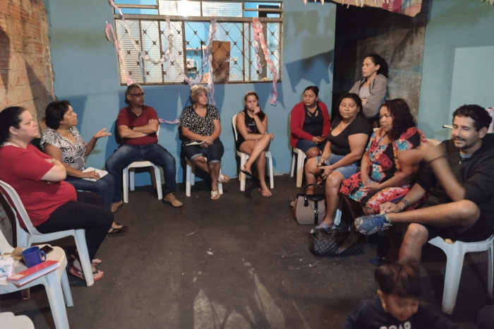 Na foto, 10 pessoas estão sentadas em roda, sendo oito mulheres e dois homens. Uma mulher está falando e gesticulando com as mãos e os demais olham para uma outra