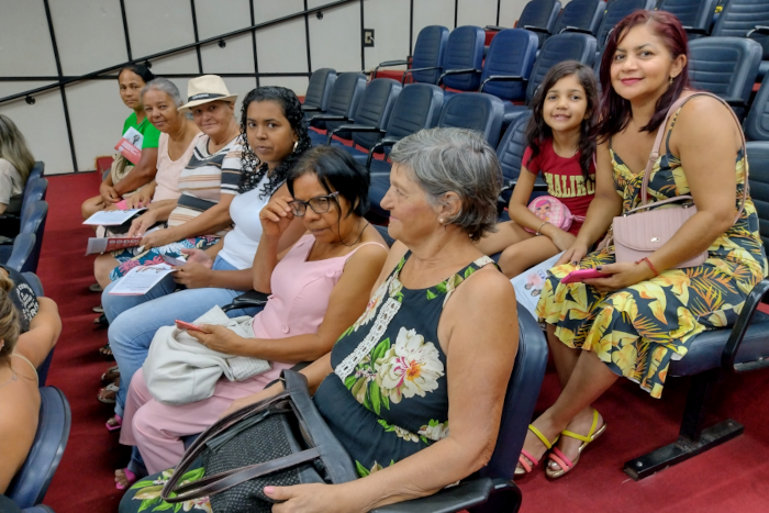 Sete mulheres e uma menina estão sentadas em poltronas pretas, estando seis delas na fileira da frente e uma, junto com a menina, na fileira de trás